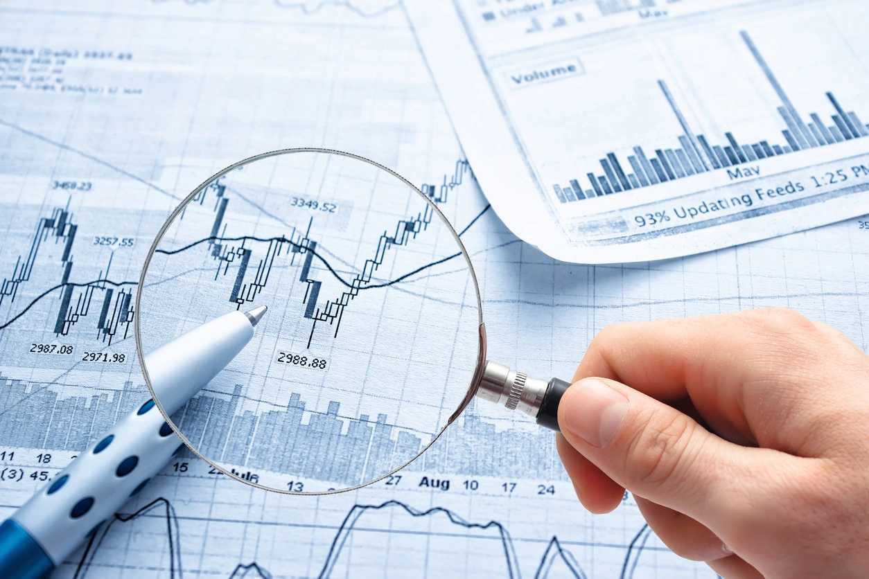 A person holding a magnifying glass over some graphs