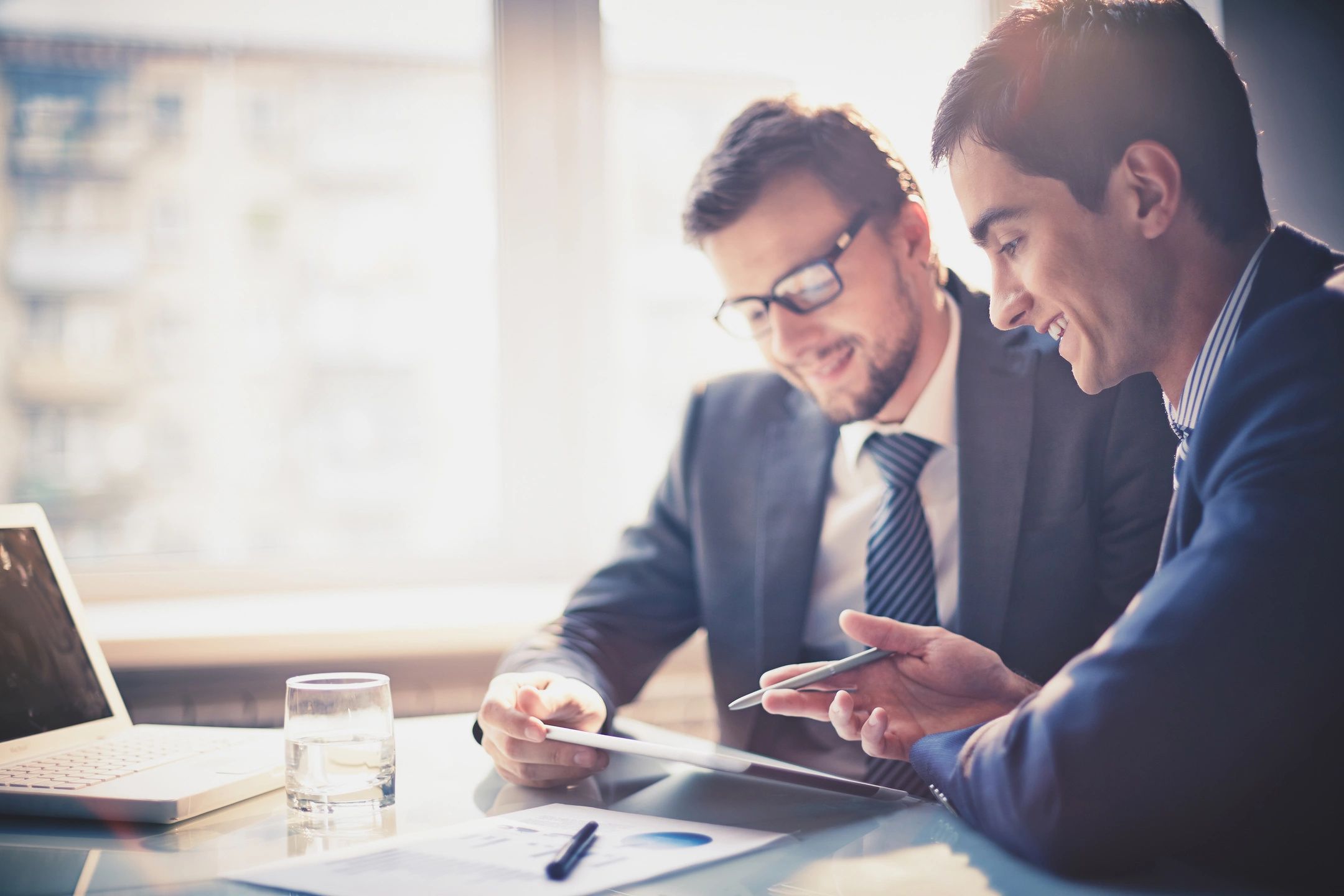 Two men in suits and ties looking at a tablet.